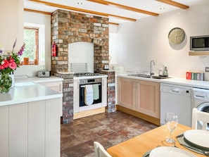 A modern kitchen with a stone fireplace, a Bosch dishwasher, and a dining area with a table set for two. - The Garden House - UK52180 (Beaworthy)