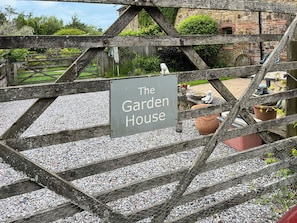 Ein Schild mit der Aufschrift 'The Garden House' hinter einem Holzzaun und einem Kiesweg.