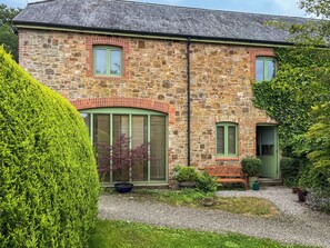 A stone building with a gravel driveway, a green door, and a bench. - The Garden House - UK52180 (Beaworthy)