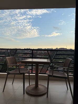 A balcony with a table and two chairs, overlooking a cityscape with buildings and a clear sky. - The Ember House_Stylish 1BR apartment in kyanja. (Kampala)