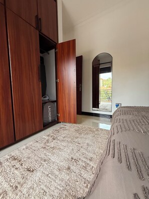 A bedroom with a bed, a wardrobe, and a mirror reflecting a view outside. - The Ember House_Stylish 1BR apartment in kyanja. (Kampala)