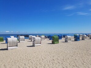 A beach with rows of wicker lounge chairs, some with numbers on them, and a clear blue sky. - A Vacation Under a Thatched Roof at the Historic Frisian House "Antje" on the North Sea Coast (Niebüll)