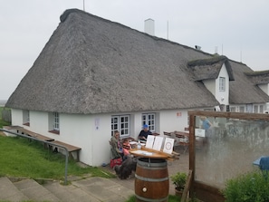En traditionell byggnad med halmtak, en träbänk utanför, ett fat och en skylt.