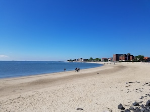 En bred sandstrand med en klarblå himmel, några få personer som promenerar och byggnader i bakgrunden.
