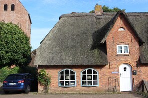 A traditional brick house with a thatched roof, two windows with white frames, and a white door. - A Vacation Under a Thatched Roof at the Historic Frisian House "Antje" on the North Sea Coast (Niebüll)