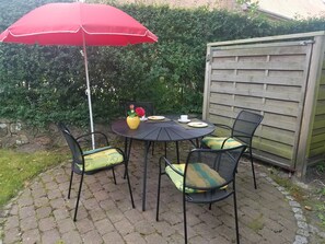 An outdoor patio with a round table, four chairs, a red umbrella, and a wooden fence. - A Vacation Under a Thatched Roof at the Historic Frisian House "Antje" on the North Sea Coast (Niebüll)