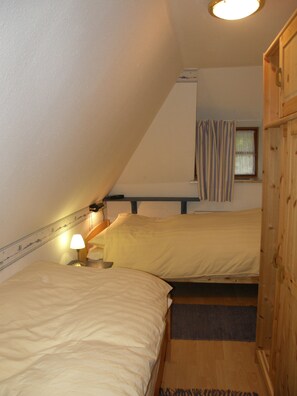 A small, narrow room with two beds, a window with curtains, and a wooden wardrobe. - A Vacation Under a Thatched Roof at the Historic Frisian House "Antje" on the North Sea Coast (Niebüll)