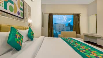 Habitación de hotel con cama, sofá, vista a edificios y un cuadro en la pared.