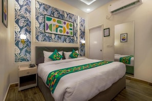 Una camera d'albergo con un letto, un comodino, opere d'arte alle pareti e un condizionatore d'aria.