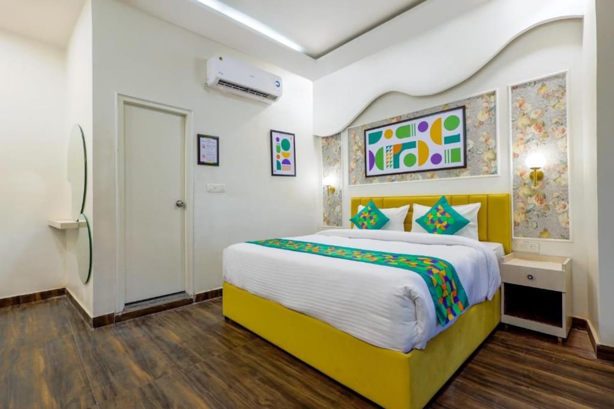 Una camera d'albergo con un letto, un comodino, un condizionatore d'aria e una parete con un quadro geometrico.