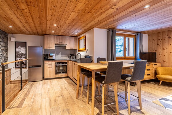 Une cuisine moderne avec des meubles en bois, un four encastré et un coin repas comprenant une table et des chaises en bois.