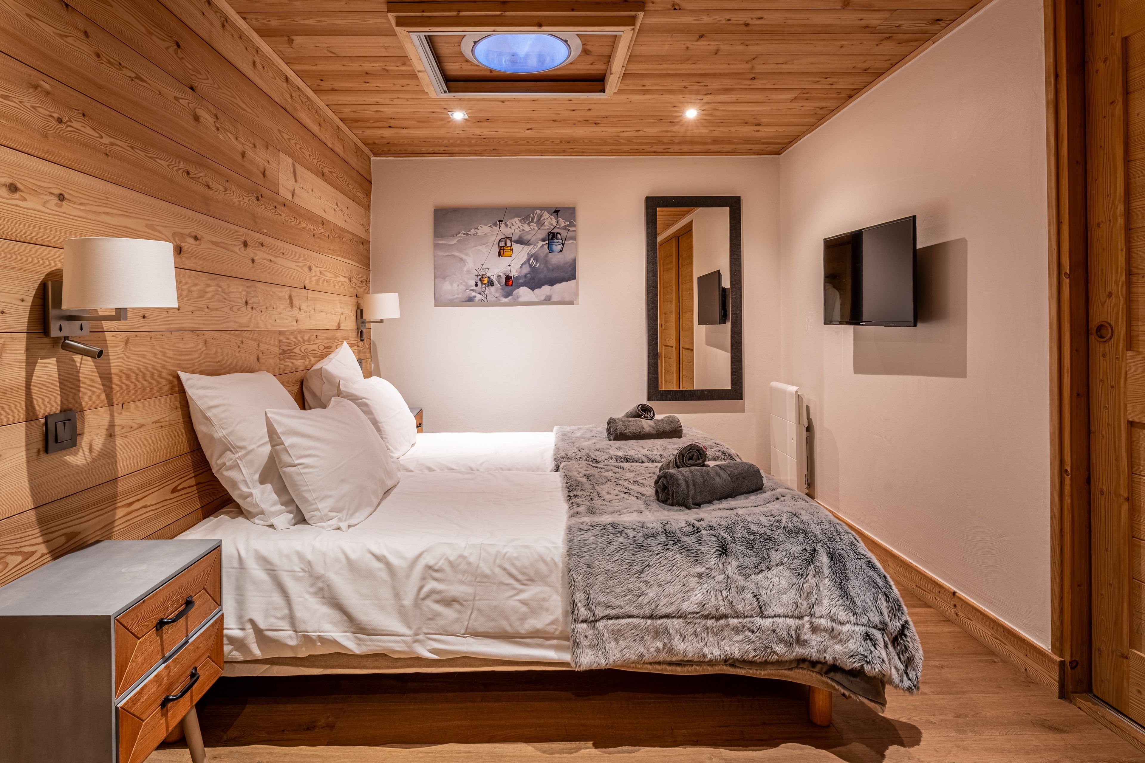 Une chambre avec un plafond en bois, un lit avec une literie blanche, un téléviseur fixé au mur et un tableau représentant un paysage de montagne.