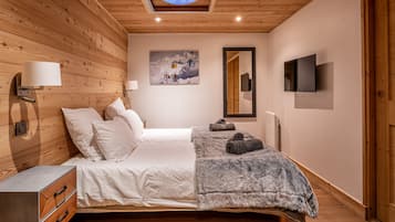 Une chambre avec un plafond en bois, un lit avec une literie blanche, un téléviseur fixé au mur et un tableau représentant un paysage de montagne.