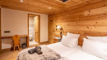 Een knus ingerichte kamer met houten plafond, een bed met witte lakens, een bureau met stoel, en een klein nachtkastje met lamp.