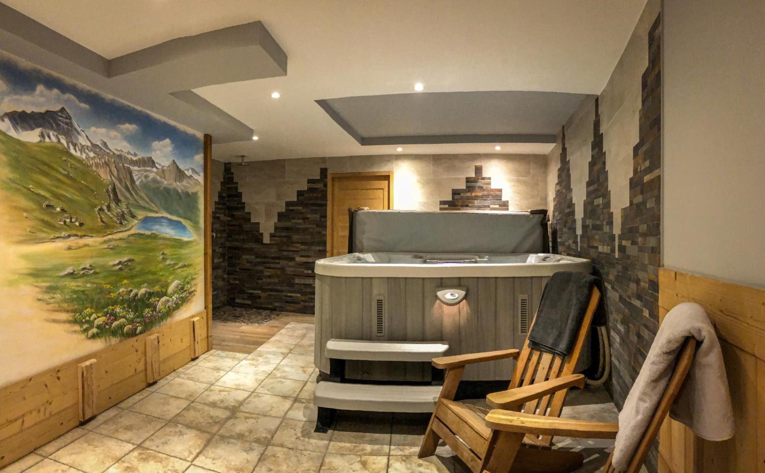 Une salle de spa équipée d’un bain à remous, d’un fauteuil en bois et ornée d’une fresque représentant un paysage montagneux.