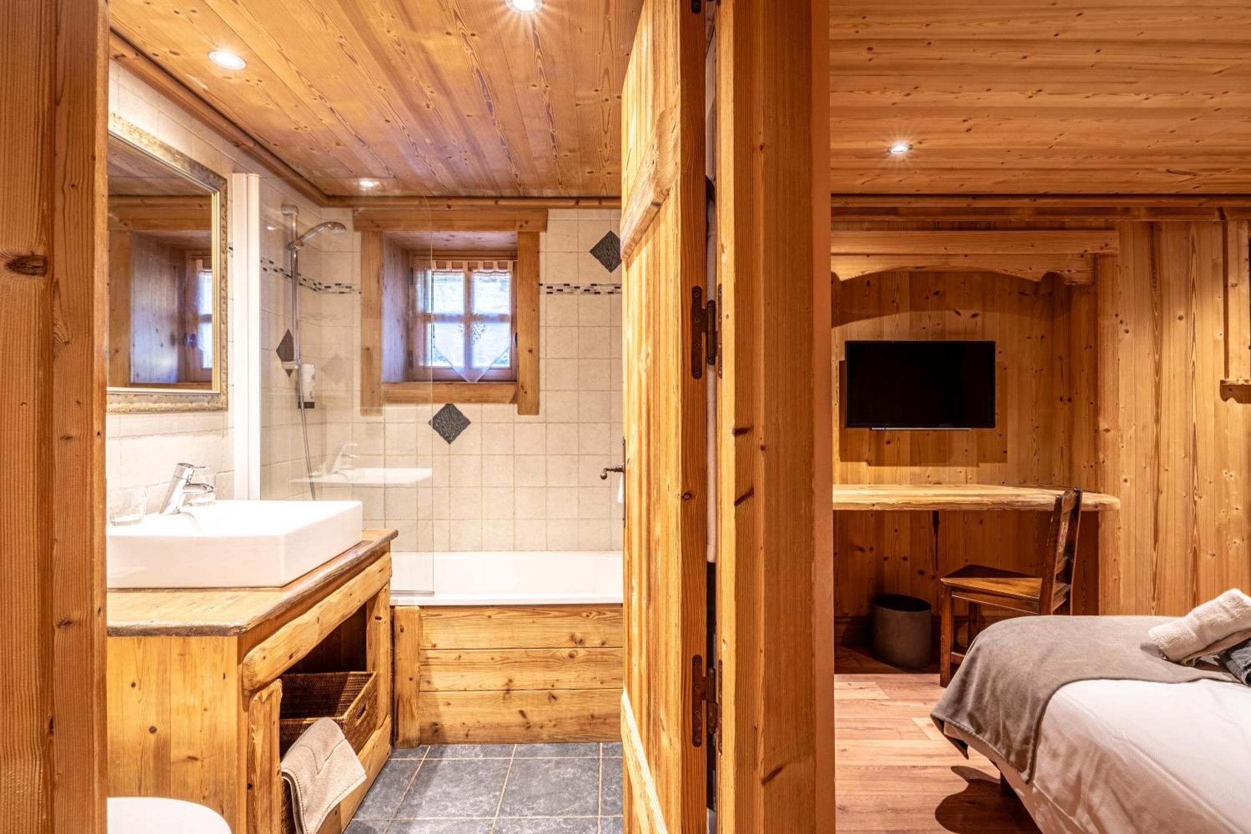 Ein Badezimmer einer Holzhütte mit Waschbecken, Spiegel, Dusche und einem Fenster.