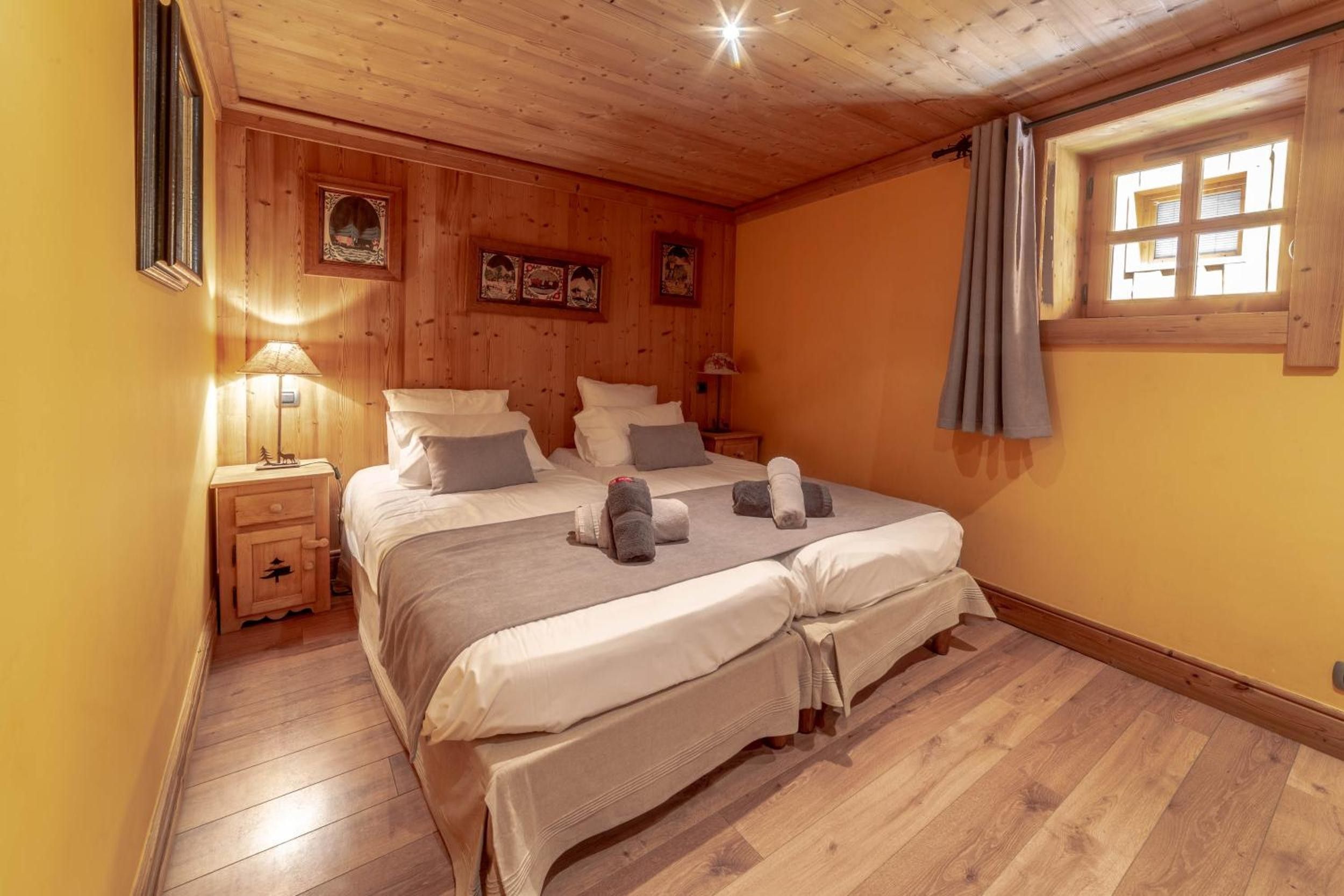 A wooden-paneled bedroom with a double bed, bedside tables, and a window with curtains.