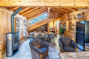 A wooden interior with a dining area, seating, and a built-in wood stove.
