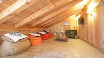 A cozy attic room with wooden beams, a small table, bean bags, and a cabinet.