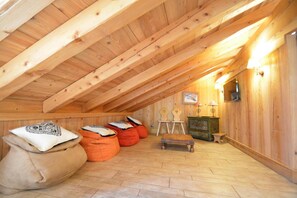 A cozy attic room with wooden beams, a small table, bean bags, and a cabinet.