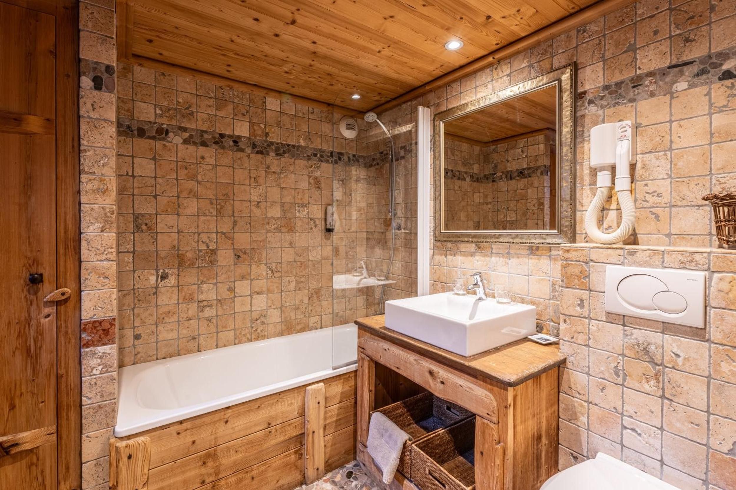 Une salle de bain avec un meuble-lavabo en bois, une baignoire blanche et un espace de douche carrelé en pierre.