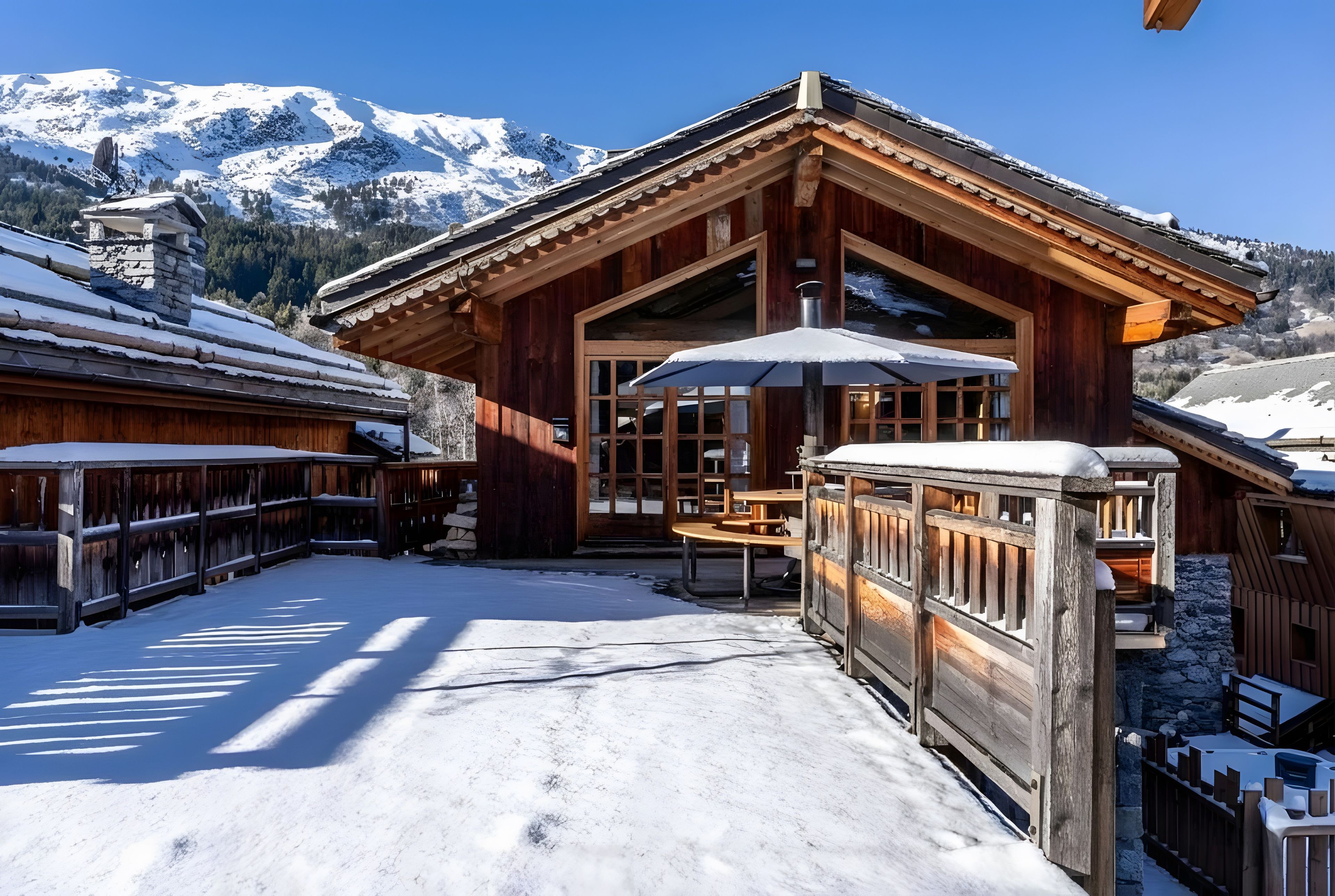 Eine Holzhütte mit schneebedecktem Dach, einer Terrassenfläche und Bergblick.