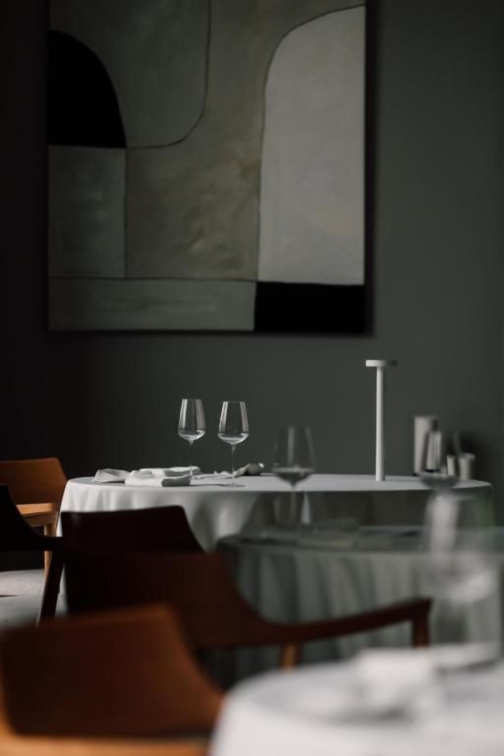 A dining area with tables set for two, each with a wine glass and a water glass.