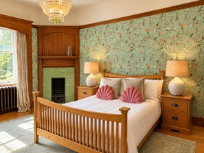 A bedroom with a wooden bed, two bedside tables with lamps, a green tiled fireplace, and floral wallpaper. - Balvonie House, Grand Scottish Mansion, Hot Tub with Island Views. 12 Bedrooms (Skelmorlie)