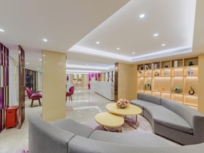 Un hall d’hôtel moderne comprenant un comptoir d’accueil, un espace salon et une bibliothèque agrémentée d’objets décoratifs.