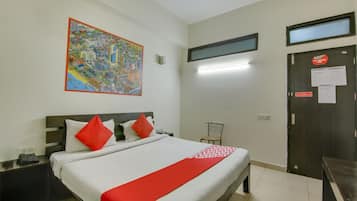 Habitación de hotel con cama, mesita de noche, televisor montado en la pared, una puerta con un cartel y un mapa colorido en la pared.