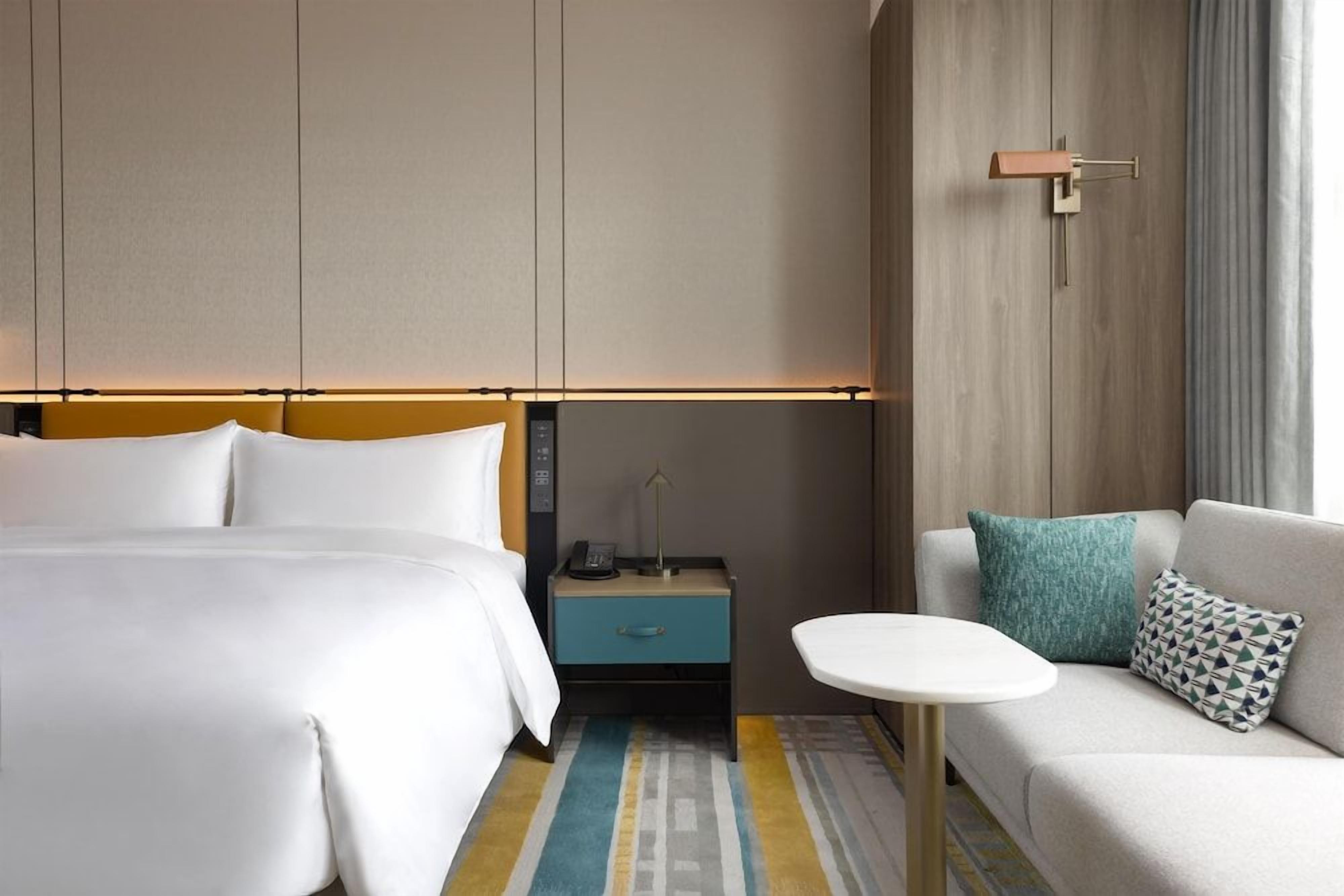 Een hotelkamer met een bed, een nachtkastje met een lamp, een bank en een kleine tafel.