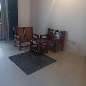 A corner of a room with two wooden chairs and a small table, a black rug, and a tiled floor. - Jalyns Resort (Puerto Galera)
