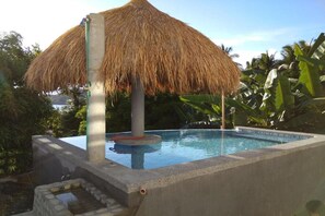 A swimming pool with a thatched roof structure, surrounded by lush greenery. - Jalyns Resort (Puerto Galera)