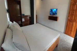 A bedroom with a bed, a television mounted on the wall, and a wooden wardrobe. - Jalyns Resort (Puerto Galera)