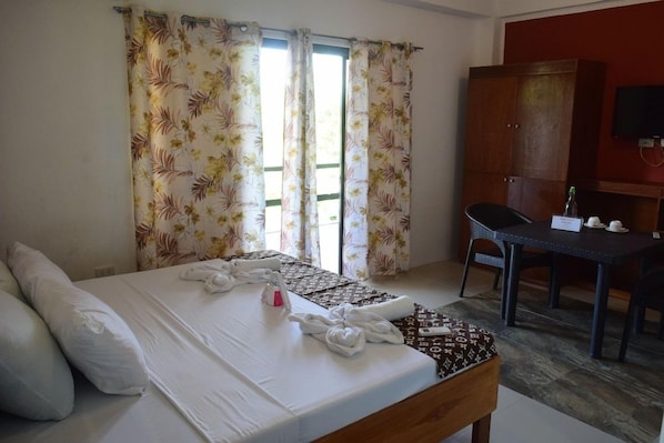 A hotel room with a bed, a desk, a chair, a wardrobe, and a television. - Jalyns Resort (Puerto Galera)