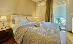 A hotel room with a bed, two bedside lamps, a window with curtains, and a view of the outside. - Hospitality Expert - Pefki Prestige Condo (Pefki)