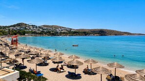 A beach with umbrellas, sun loungers, and a lifeguard tower. - Hospitality Expert - Pefki Prestige Condo (Pefki)