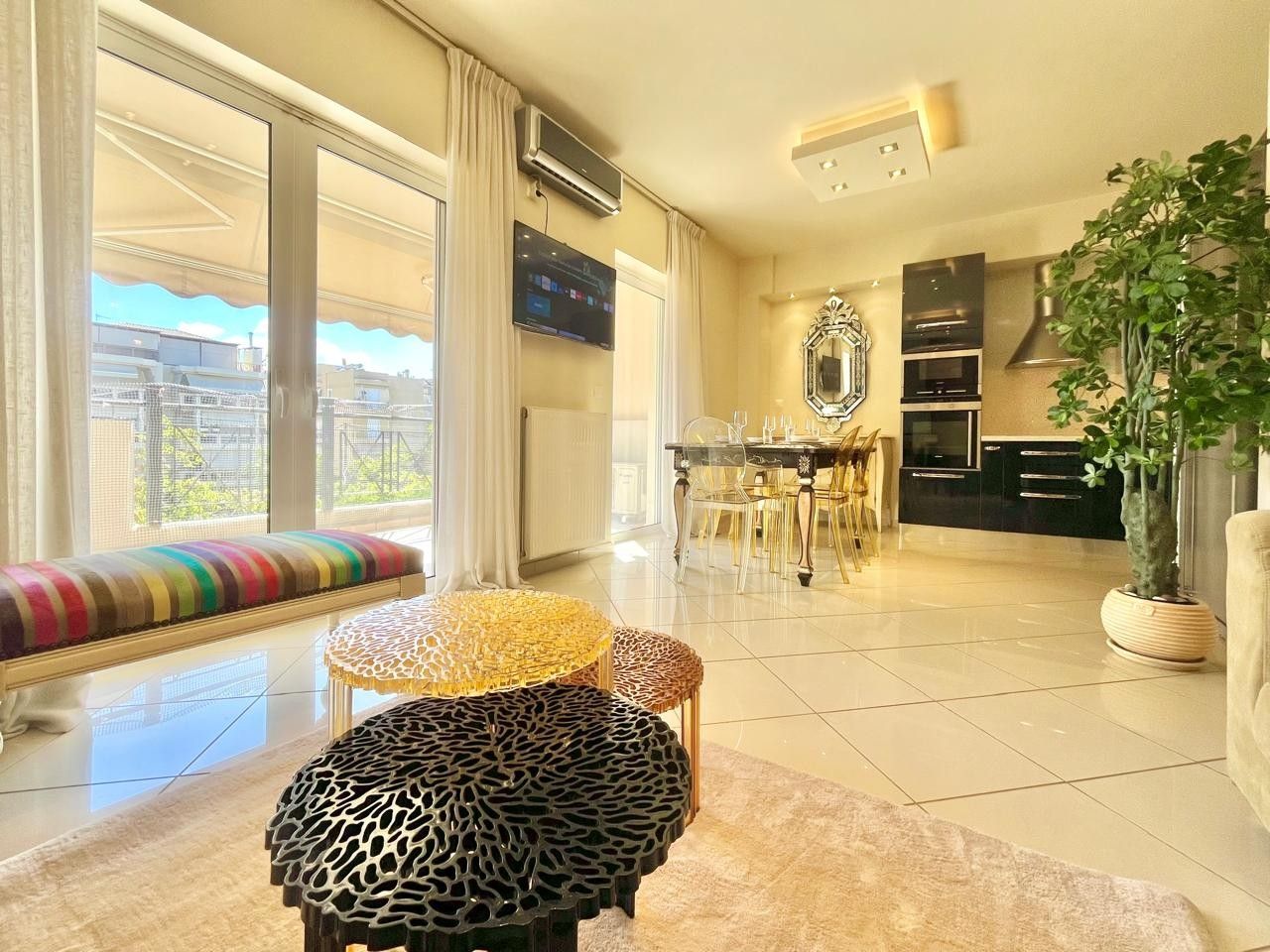 A spacious living area with a large window, a dining table with chairs, and a kitchen area.