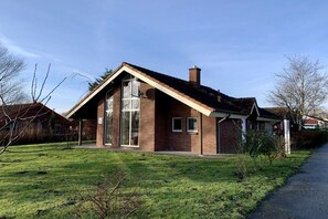 Uma casa térrea de tijolos, com telhado inclinado, uma janela grande e chaminé aparente.