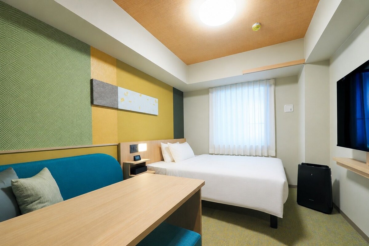 Une chambre d’hôtel équipée d’un lit, d’un bureau, d’une chaise, d’une télévision et d’une fenêtre avec des rideaux.