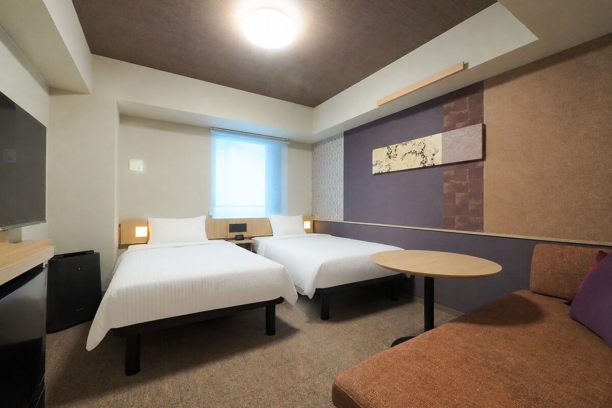 Une chambre d’hôtel avec deux lits, un bureau, une chaise, une petite table et un téléviseur.