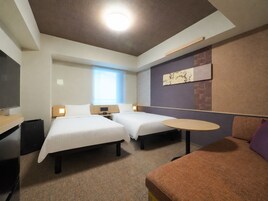 Habitación de hotel con dos camas, un escritorio, una silla, una mesita y un televisor.