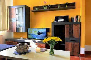 Une pièce comprenant une télévision, un meuble en bois, une étagère avec des objets décoratifs et un vase rempli de fleurs.