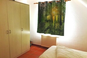 A bedroom with a wardrobe, a radiator, and a window with a forest-themed curtain. - Holiday apartment with 2 bedrooms (Bakenberg)