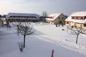 Pátio coberto de neve com edifícios, árvores secas e c éu limpo.