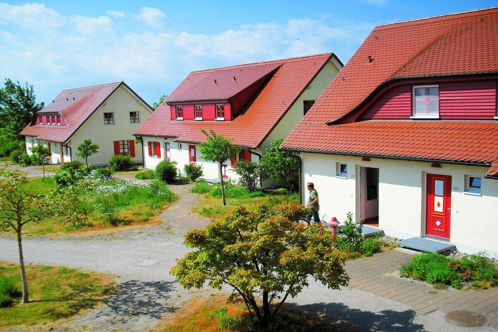Een rij huizen met rode daken en witte muren, een geplaveid pad en begroeiing.