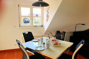 A dining area with a table set for two, chairs, a window with artwork, and a ceiling lamp. - Holiday apartment with 2 bedrooms (Bakenberg)