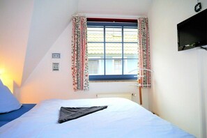 A bedroom with a bed, a window with curtains, a radiator, and a television mounted on the wall. - Oak Park W 3.5||Ostseebad Prerow (Ostseebad Prerow)