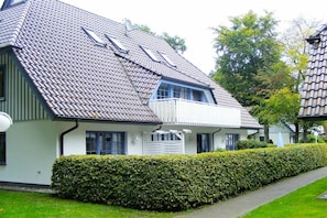 Ein zweistöckiges Haus mit geneigtem Dach, einem Balkon und einer gepflegten Hecke.