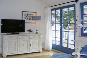 Ein Zimmer mit Fernseher auf einem weißen Schrank, einer Lampe und Blick durch eine blaue Tür.